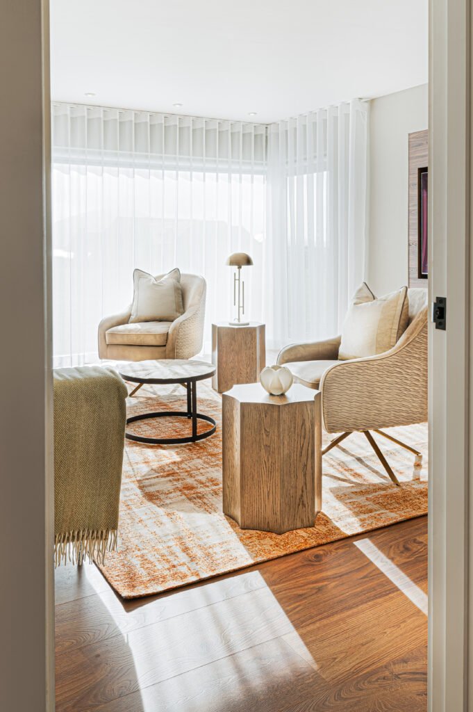 Bright sitting room viewed through doorway with paired armchairs, wooden side tables and orange rug, Rosscarbery Reading Room, AK Interior, Cork.