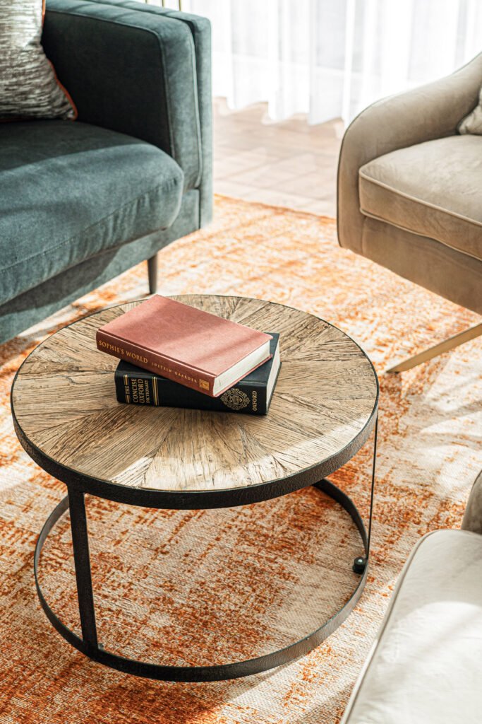 Styled timber coffee table with stacked books on an orange rug beside green sofa.