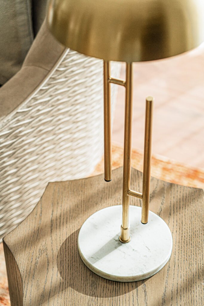 Detail of woven armchair arm and brass lamp creating layered textures.