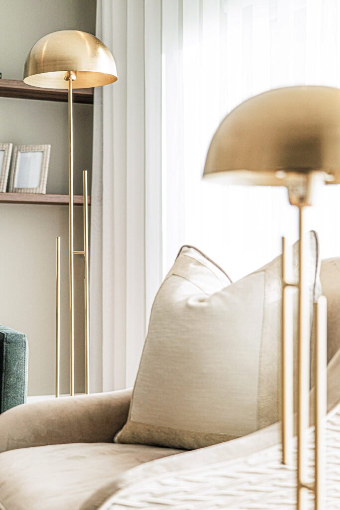 Close-up of neutral armchair with layered cushions and twin brass floor lamps, sheer curtains behind, Rosscarbery Reading Room, AK Interior, Cork.