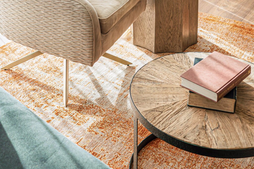 Close-up of round coffee table on orange rug with books and black metal base.