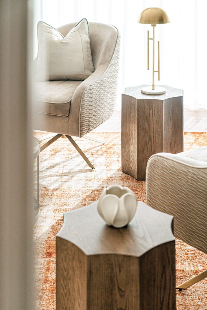 Neutral armchairs with brass table lamp and sculptural vase on wooden side tables, orange patterned rug, Rosscarbery Reading Room, AK Interior, Cork.