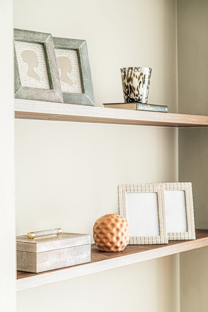 Floating shelves with framed silhouettes, candle and decorative box on soft neutral wall.