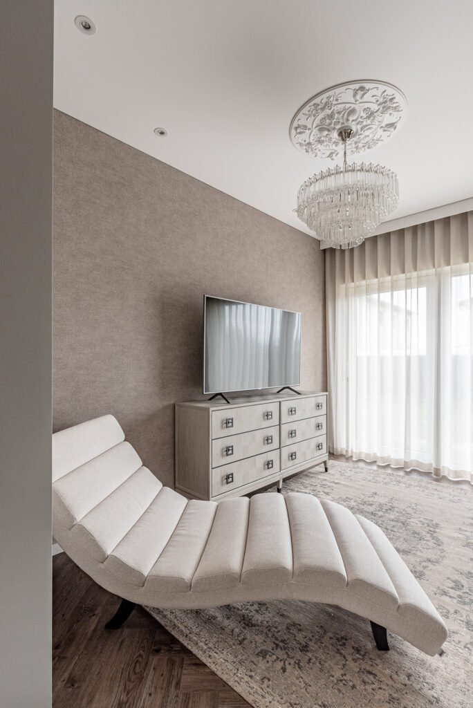 Elegant relaxation corner with a cream chaise lounge, crystal chandelier and large window bringing in natural light – AK Interior, Monkstown Full House Design