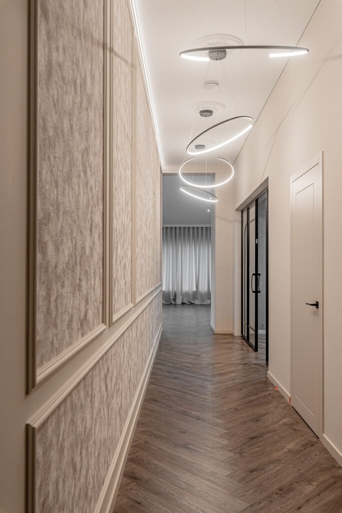 Long hallway with modern ring-shaped lighting and textured wall panels. Project Monkstown Full House Design – AK Interior.