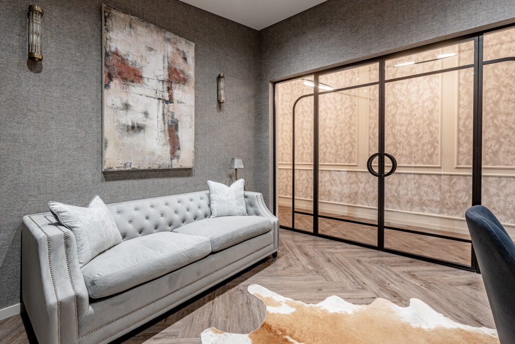 Elegant lounge area with a grey sofa, artwork, and glass partition doors. Project Monkstown Full House Design – AK Interior.