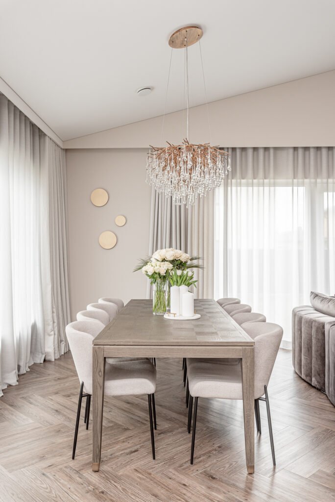 Dining area with soft upholstered chairs and a large crystal chandelier. Project Monkstown Full House Design – AK Interior.