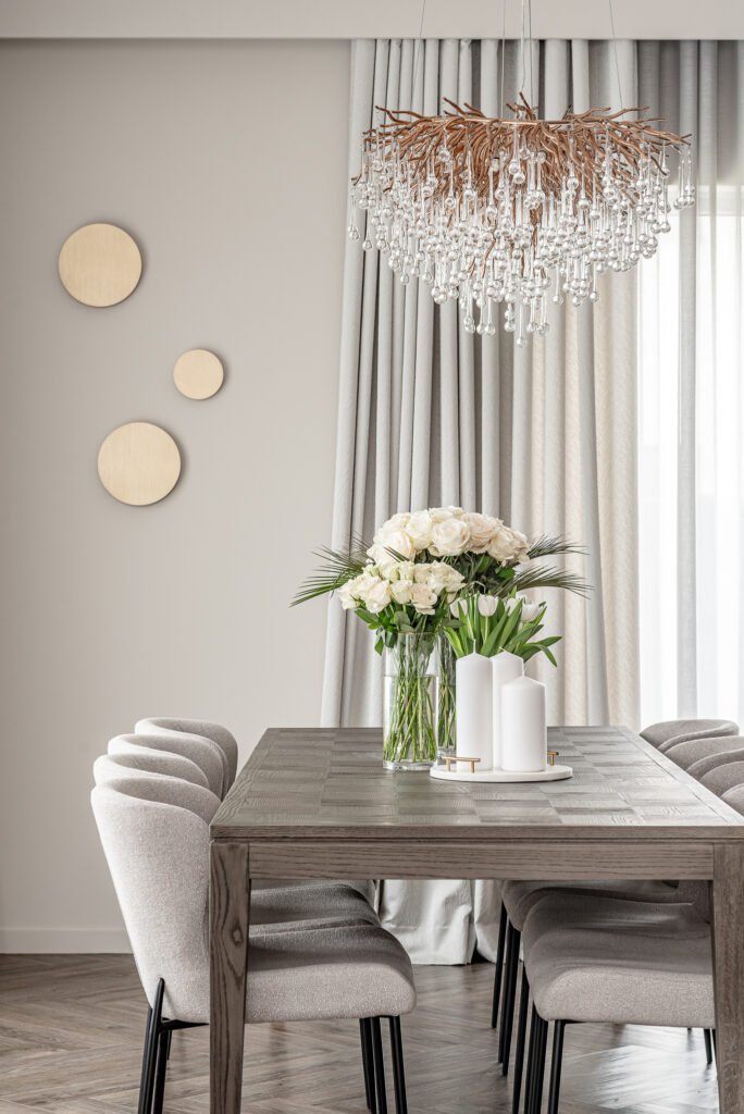 Dining table with a white rose bouquet and an elegant crystal chandelier. Project Monkstown Full House Design – AK Interior.