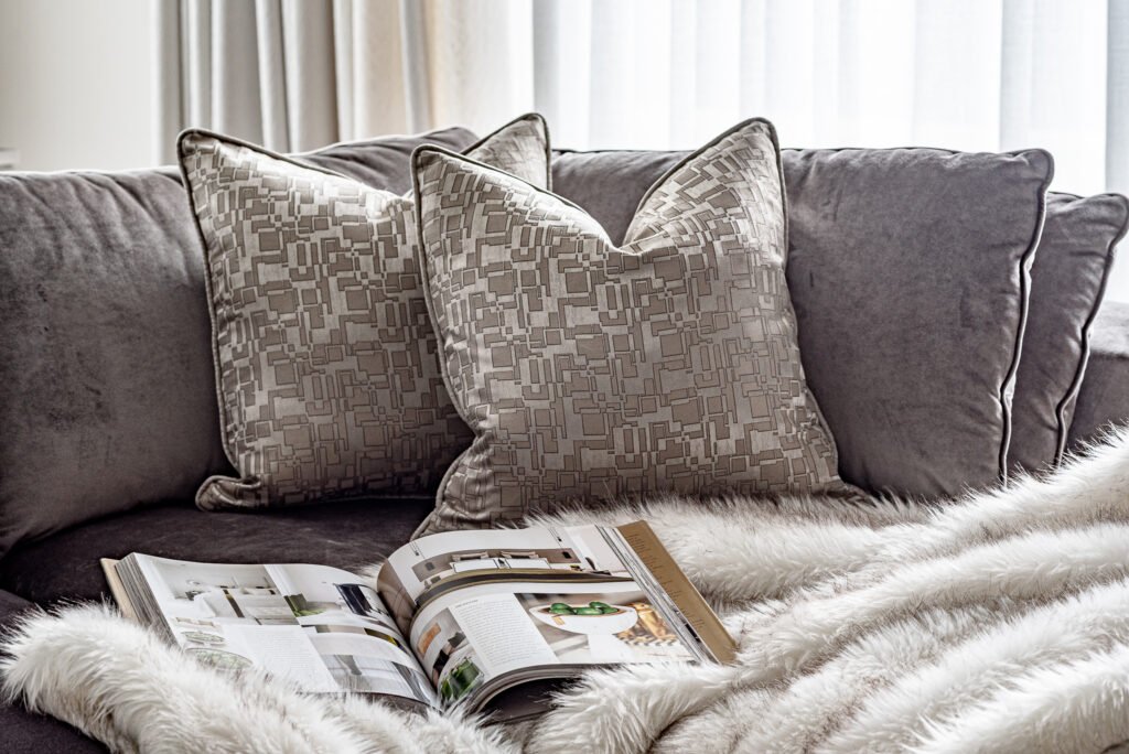 Grey velvet sofa with decorative cushions and an open magazine. Project Monkstown Full House Design – AK Interior.